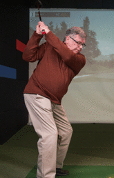 John Mac Donald swinging golf club at a golf simulator.