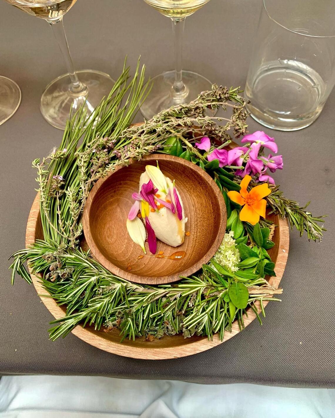 A closeup of a beautiful plate of food styled with flowers and herbs around the edges and a small plate in the centre.