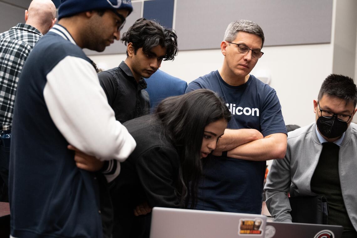 A group of students stand around a computer showing a judge a project