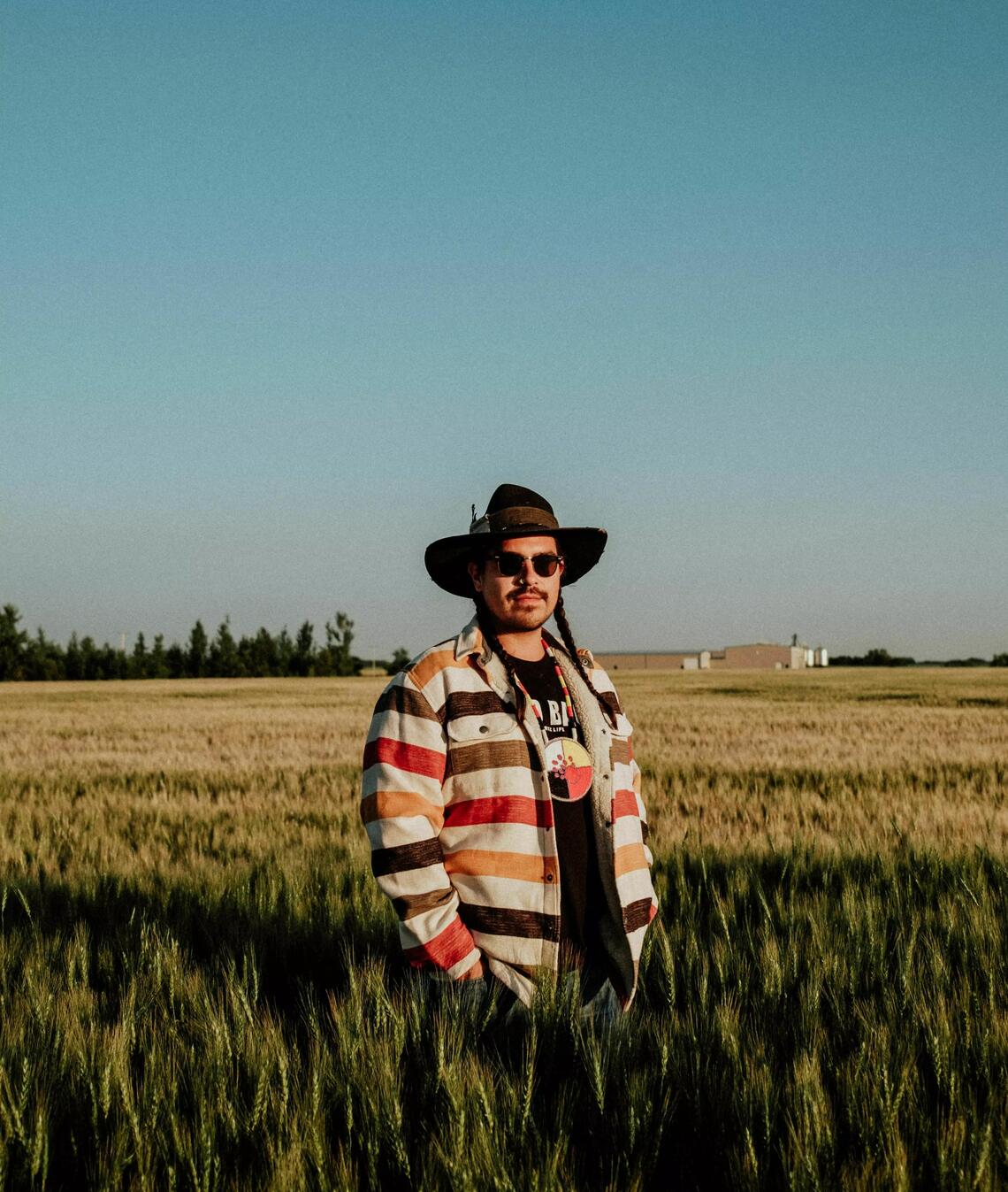 A man wearing a striped shirt and large hat stands in a field