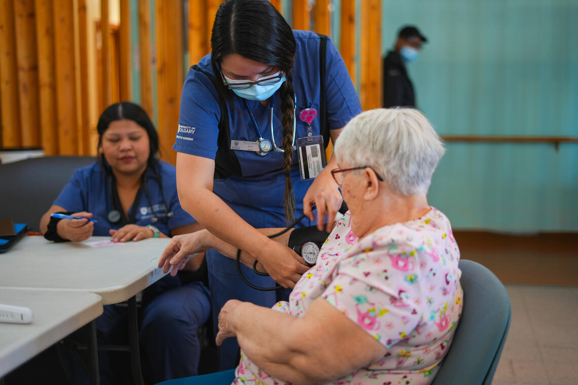 nursing student takes blood pressure of a woman while another student looks on