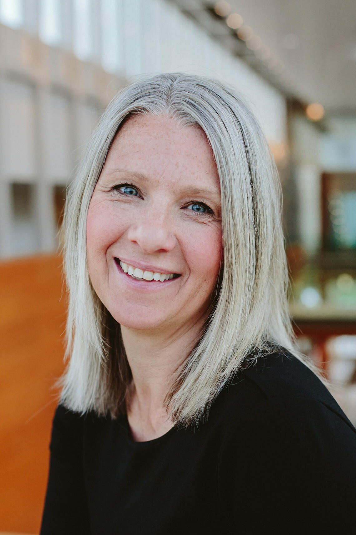 Natasha Kenny, a white woman with straight grey hair, wearing a black shirt and smiling inside the Taylor Institute for Teaching and Learning.