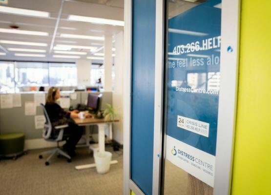 An image looking into the DCC call centre, with a person sitting at a desk taking a call just out of focus, the main focus is the glass panel reading Distress Centre Calgary