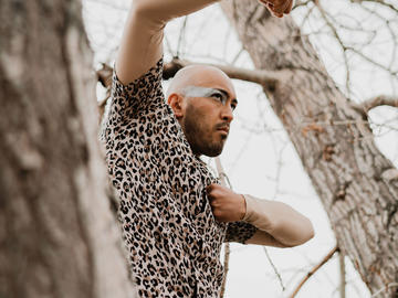 A dancer wearing a leopard print shirt poses in the forest