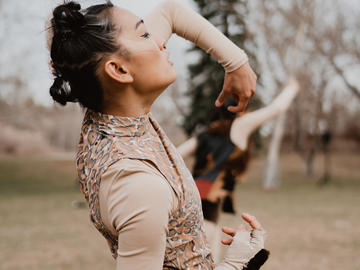 A dancer wearing a leopard print jumpsuit poses in a field