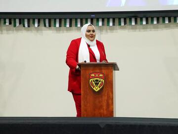 A person in a red outfit stands behind a podium on stage