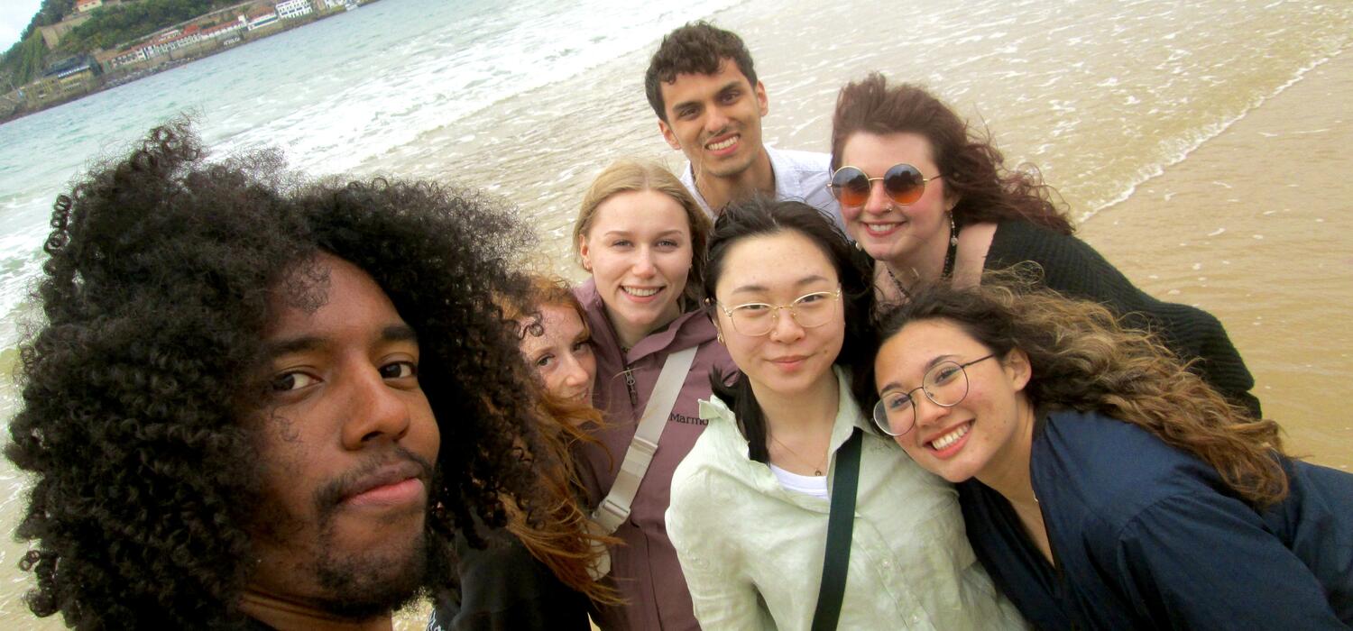 A group of diverse students pose for a selfie on a beach in Spain.