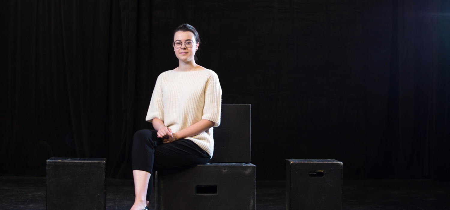 Woman sits on boxes on a stage