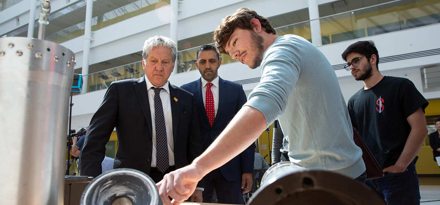 Ben Hewitt (left) and Seyedarmin Seyed-Agha-Zadeh, Schulich School of Engineering students and members of Student Organization for Aerospace Research (SOAR), show components of a rocket to Minister Dan Vandal and MP George Chahal at the funding announcement on June 26, 2023