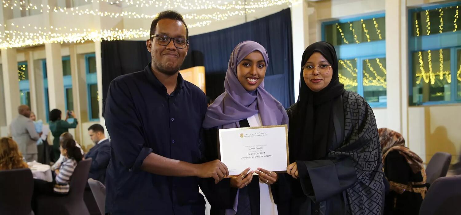 Two people stand next to a woman holding a degree, they all smile at the camera
