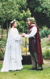 Alumnus Jonathan Love and an actress stand in front of a wooded area wearing Shakespearean garb. They are holding hands and both have flower crowns.