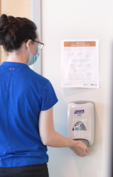 A woman uses a wall mounted hand sanitizer dispenser