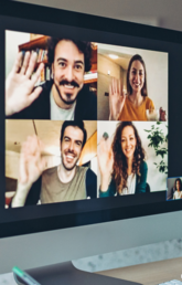 A woman smiles and waves to a computer screen showing group of people in an online meeting.