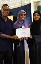 Three people stand and smile at the camera holding a degree