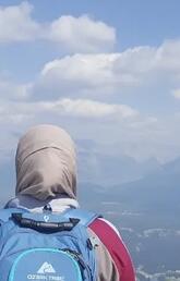 The back of a woman wearing a hijab and backpack looking out over a mountain view.