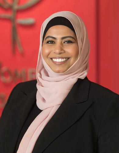 Fouzia Usman, a woman with olive skin, is wearing a pink hijab and black blazer. She is smiling.